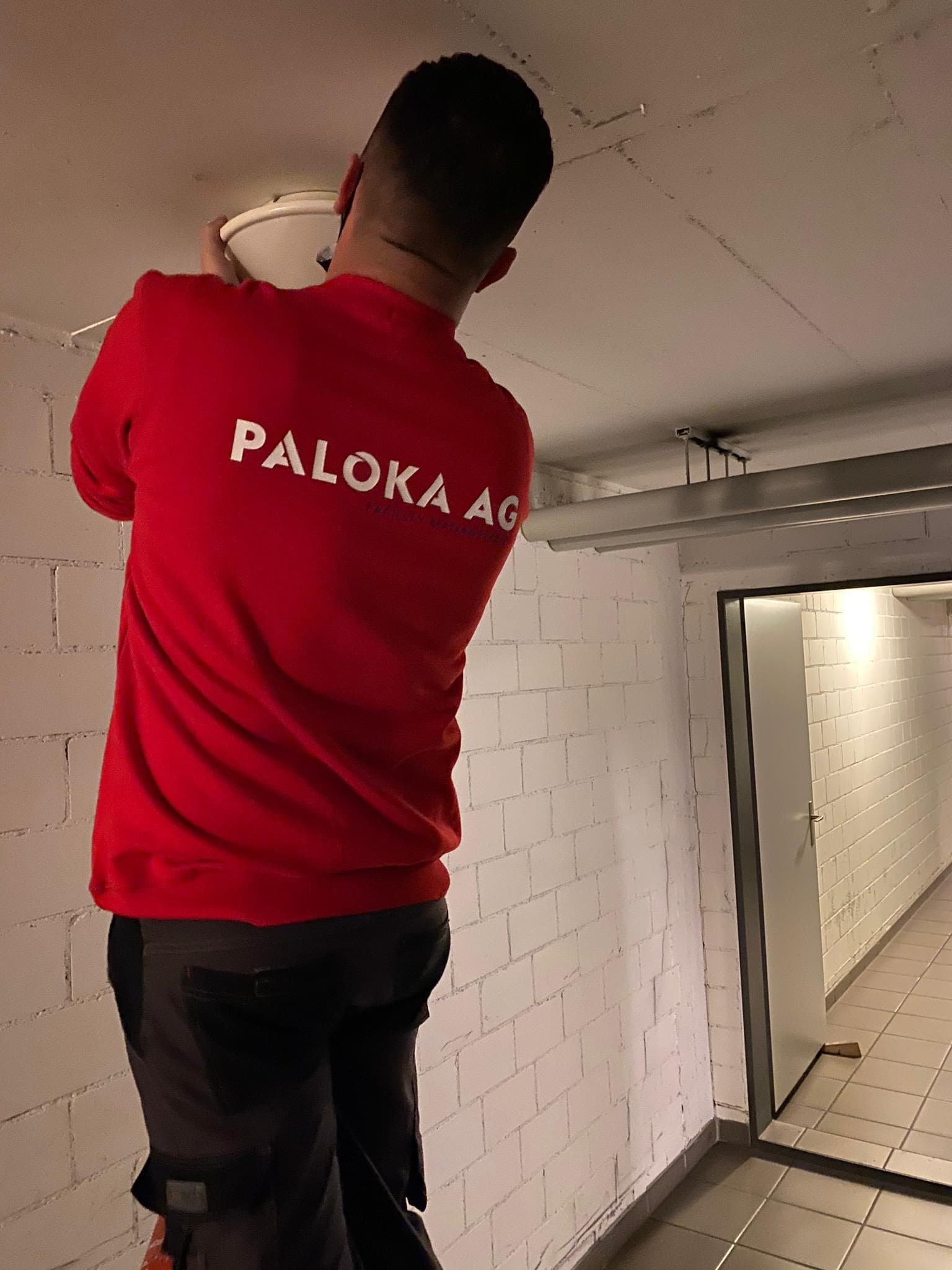 Ein Paloka-Mitarbeiter arbeitet an einer Deckenleuchte im Untergeschoss einer Liegenschaft.