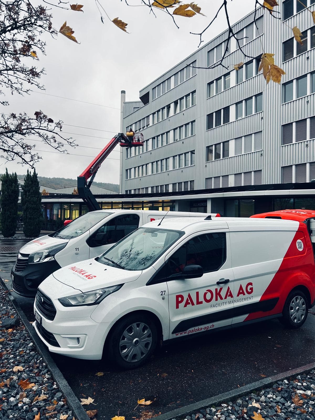 Zwei Paloka-Servicefahrzeuge vor einem mehrgeschossigen Gebäude, an dessen Fassade eine Hebebühne eingesetzt wird.