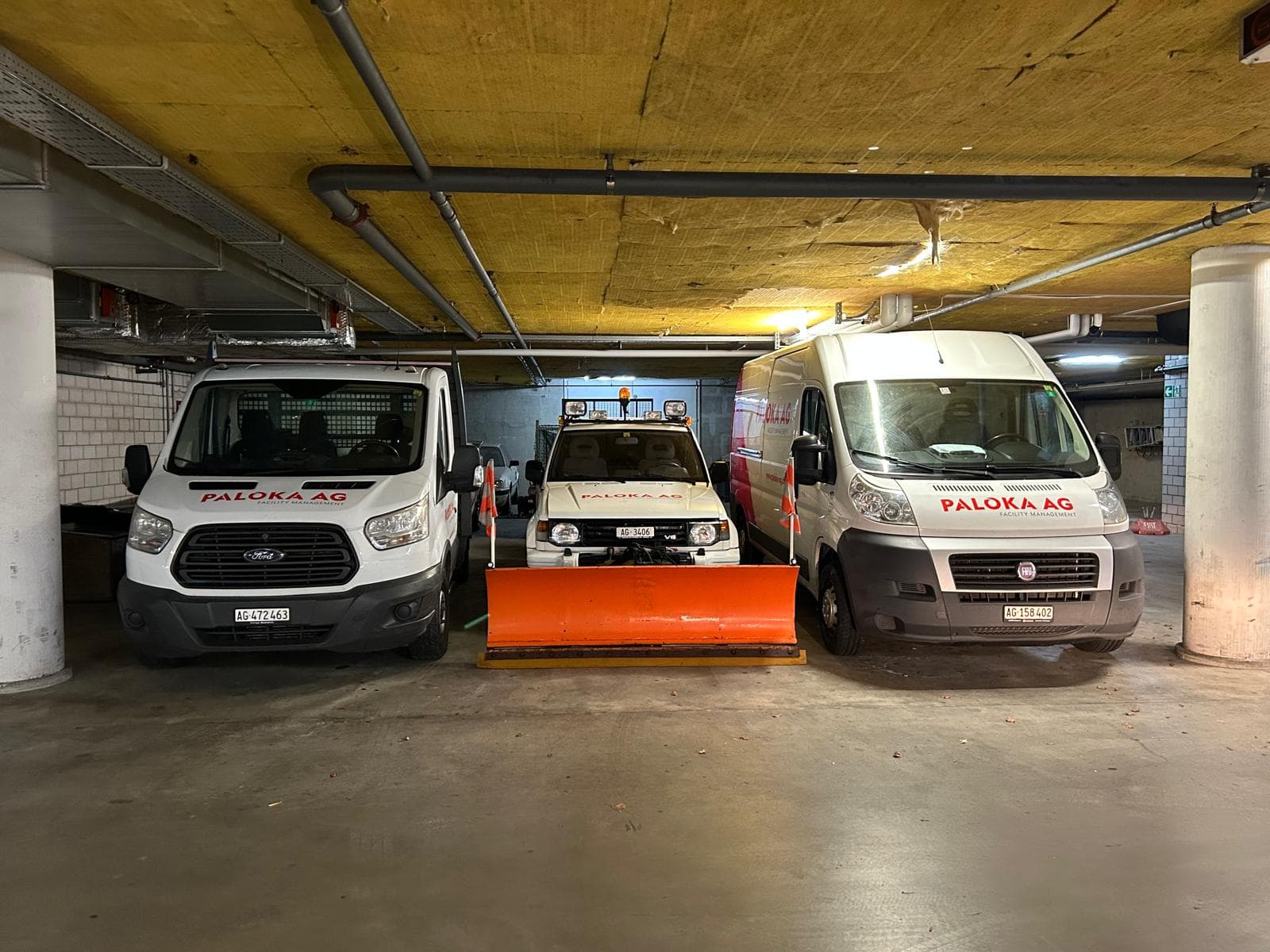 Drei Paloka-Fahrzeuge in einer Garage, darunter ein Fahrzeug mit montiertem Schneepflug.