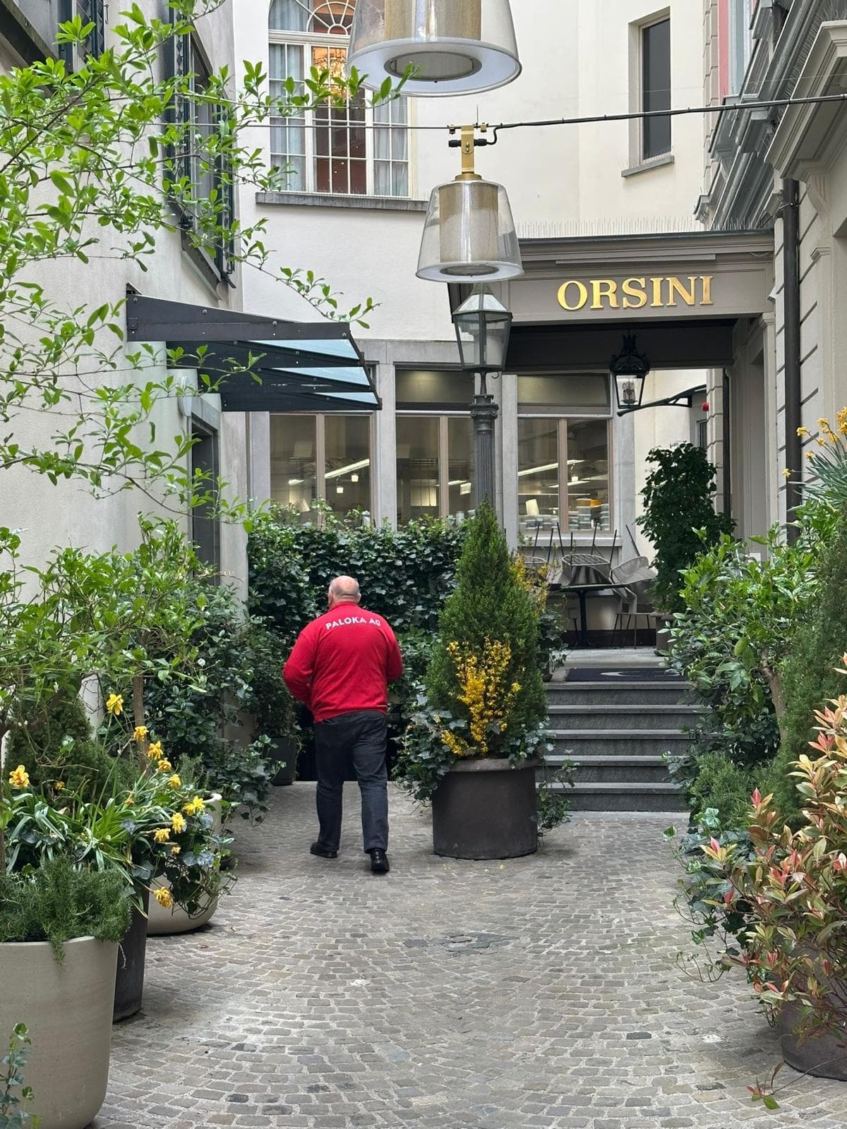 Ein Paloka-Mitarbeiter geht durch einen begrünten Innenhof mit Pflanzkübeln und einem gepflasterten Weg.