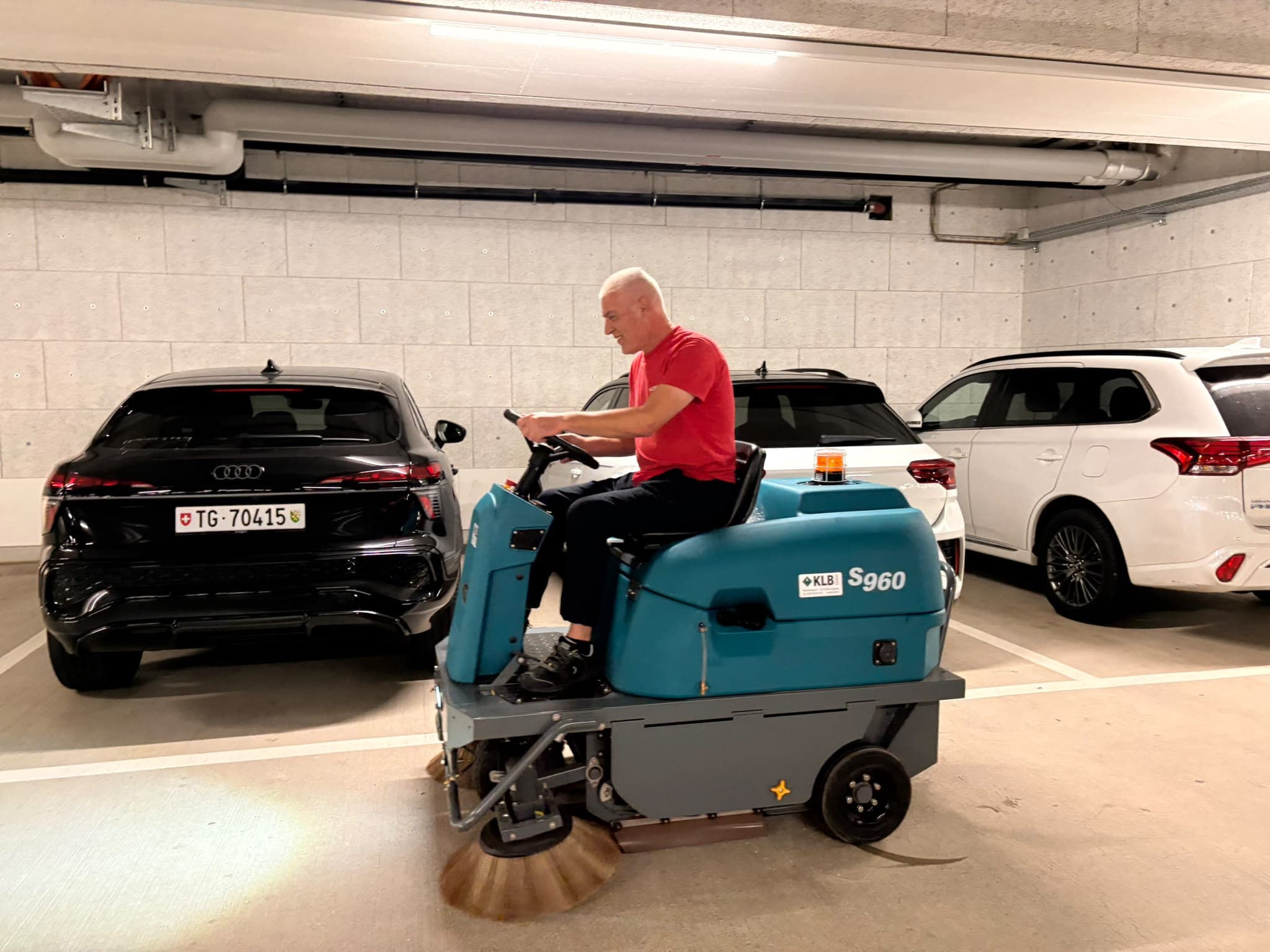 Ein Paloka-Mitarbeiter auf einer Aufsitzkehrmaschine reinigt eine Fahrbahn zwischen den Parkplätzen einer Tiefgarage.