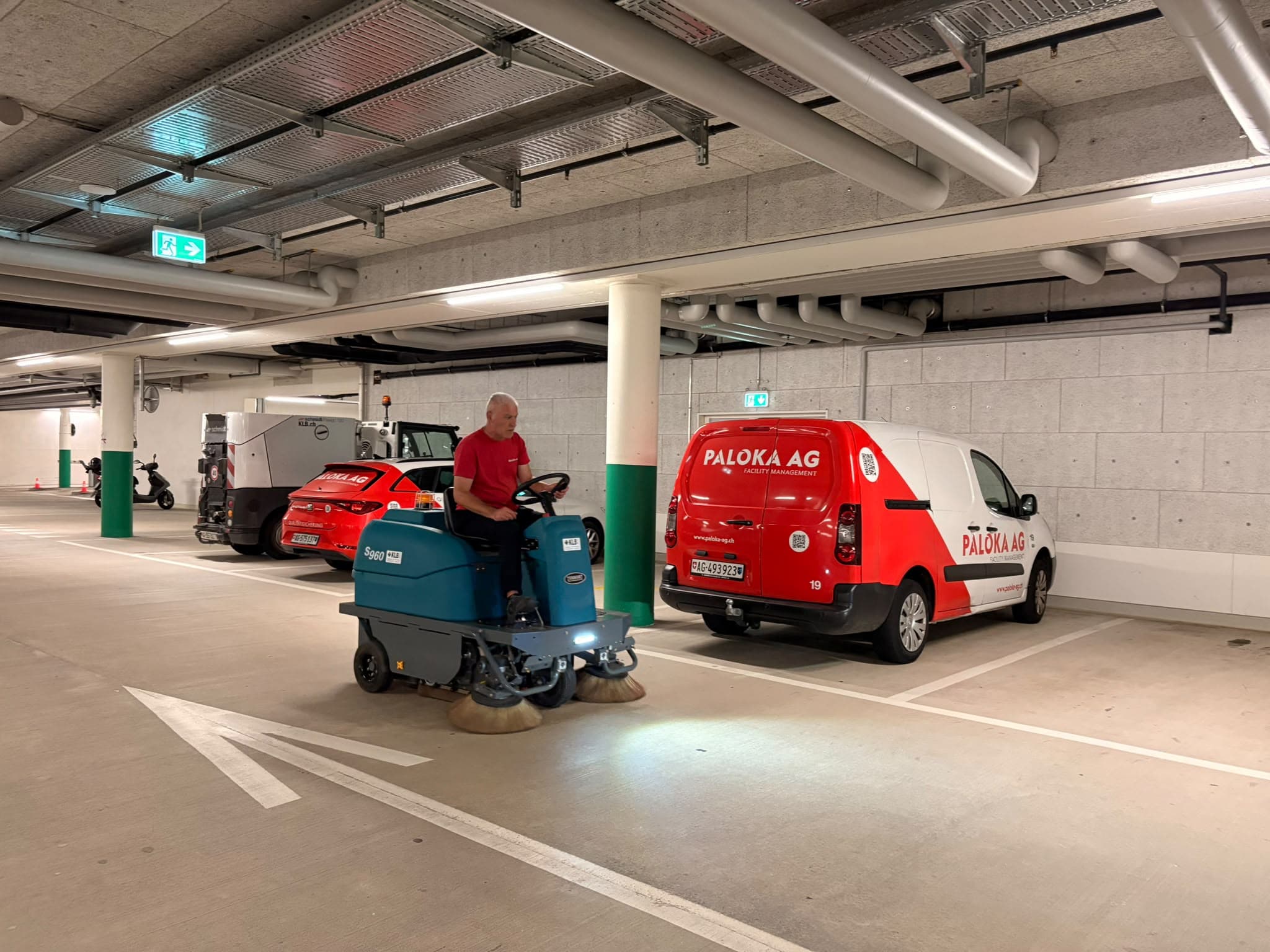 Ein Paloka-Mitarbeiter fährt eine Aufsitzkehrmaschine durch eine Tiefgarage. Dahinter stehen beschriftete Paloka-Fahrzeuge.