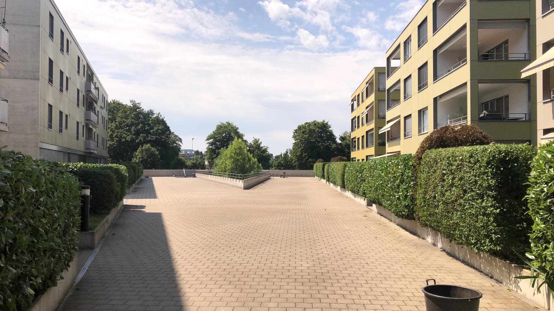Gepflasterte Wege und geschnittene Hecken zwischen den Mehrfamilienhäusern einer Wohnanlage.