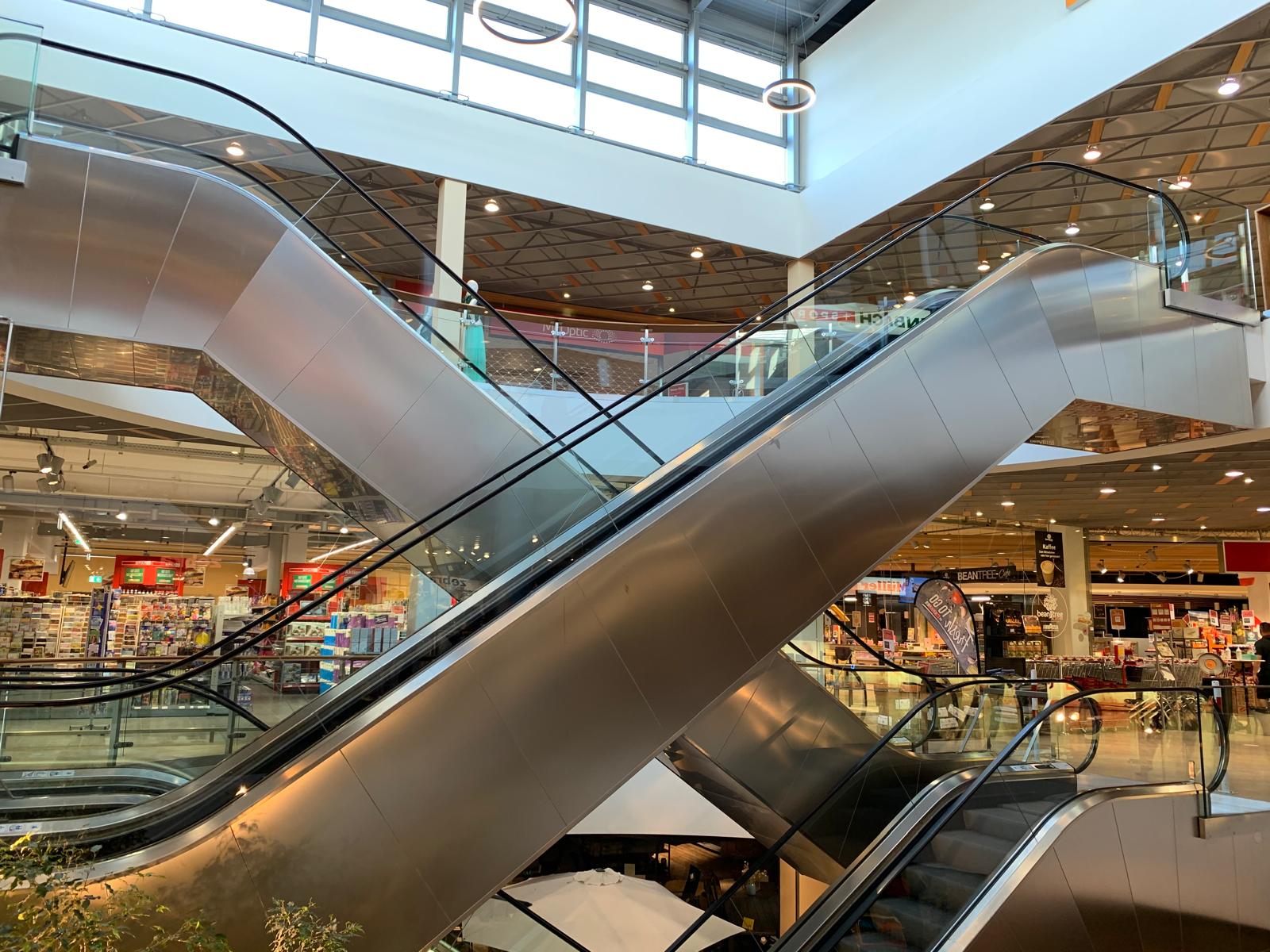 Sich kreuzende Rolltreppen und Glasgeländer unter dem hellen Oberlicht eines Einkaufszentrums